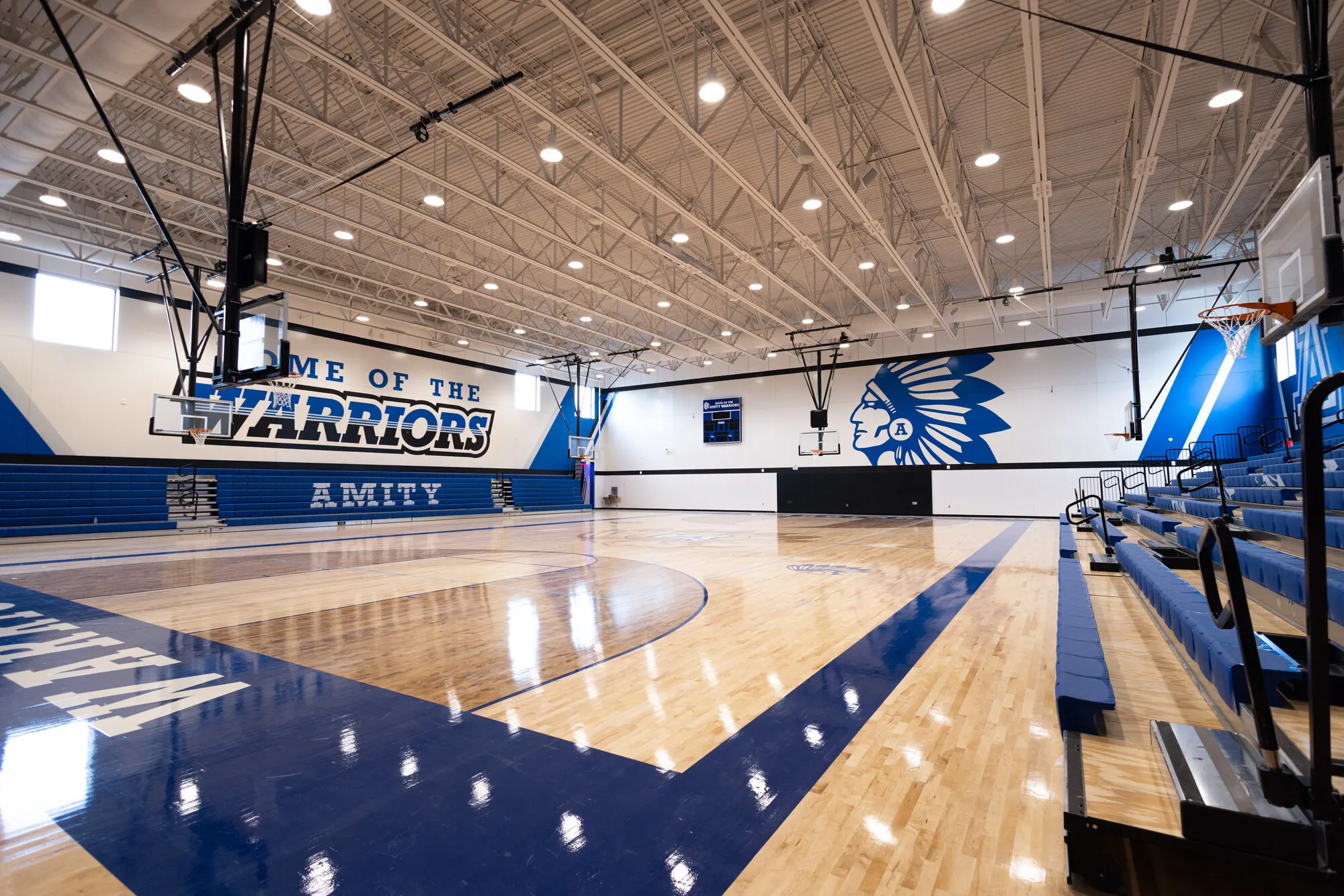 The new Amity High School gym: a polished wood court, blue bleachers, and a "Home of the Warriors" wall.
